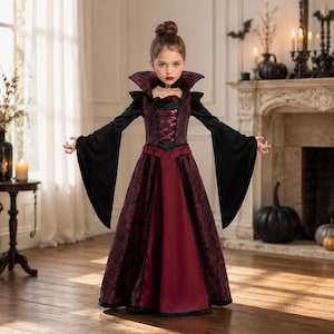 May include: A floor-length dress featuring a dark red and black damask pattern, a high standing collar, long flared sleeves, and a corset-style bodice with red ribbon lacing. The skirt has a solid deep red panel at the front and a black choker.