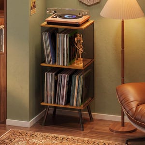 May include: A two-tier wooden record storage stand with a black metal mesh frame and four angled legs. The top surface holds a record player, while the two shelves are filled with vinyl records. A small wooden abstract sculpture sits on the top shelf.