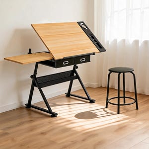 May include: A drafting table with a light wood grain surface, an adjustable tilted top, and a black metal frame. It features two black drawers, a side extension, and a black storage tray. A matching black stool with four legs sits nearby.