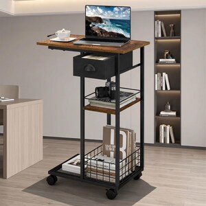May include: A mobile side table with a dark wood-grain top and a black metal frame. It features a top drawer, a middle shelf, and a bottom wire storage basket. The unit is supported by four caster wheels and holds a laptop, camera, and books.