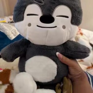 Puede incluir: Un peluche con un personaje de dibujos animados con cuerpo gris, cara blanca y detalles blancos. El juguete tiene los ojos cerrados, una nariz negra y una expresi&oacute;n sonriente. El peluche es suave y tierno.