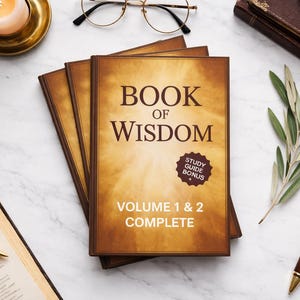 May include: Three books titled "Book of Wisdom" with "Volume 1 & 2 Complete" text. A lit candle in a gold holder, a pen, glasses, and a sprig of greenery are arranged on a marble surface.