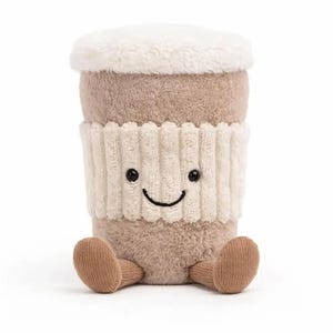 May include: A soft toy coffee cup with a smiling face, a brown body, and a cream-coloured lid. It has a cream-coloured ribbed sleeve and small brown feet. The toy is designed to sit upright.