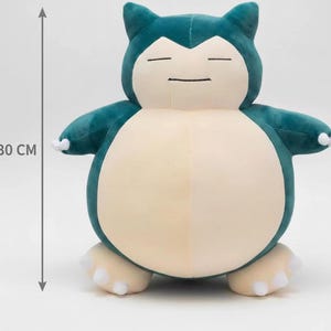 May include: A plush toy of a cartoon character, approximately 12 inches tall. The toy is teal and cream-colored, with a rounded body, small arms, and feet. It has closed eyes and a small, smiling mouth. The toy is designed to resemble a popular character.