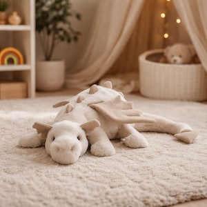 Puede incluir: Un juguete de dragón de peluche color crema con alas y espinas dorsales color beige descansa sobre una alfombra texturizada. El dragón tiene una textura suave y está diseñado para niños. El juguete tiene una paleta de colores neutros, adecuada para una guardería.