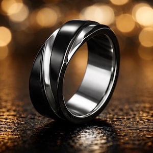 May include: A close-up of a black and silver ring. The ring has a twisted design with a black band and a silver band. The ring is on a reflective surface with blurred lights in the background.