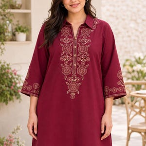 May include: A deep burgundy tunic featuring a collared neckline with a button-down placket. The garment is adorned with intricate gold-toned floral embroidery along the front placket and the cuffs of the three-quarter length sleeves.