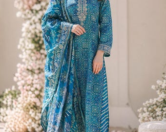 Op de afbeelding: Een vrouw draagt een blauw patroon salwar kameez, een traditionele Zuid-Aziatische outfit. De outfit bestaat uit een tuniek met lange mouwen, een bijpassende broek en een sjaal. De outfit heeft ingewikkelde borduursels en een geometrisch ontwerp. De vrouw draagt hoge hakken.