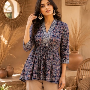 May include: A navy blue peplum-style blouse featuring a repeating floral pattern in shades of red, white, and light blue. The top has a V-neckline, three-quarter length sleeves, and a drawstring waist tie that gathers the fabric at the midsection.