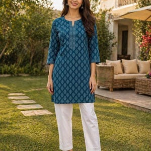 May include: A teal tunic and white pants set. The tunic features a detailed leaf pattern and a split neckline. The three-quarter sleeves and the pants' hem are adorned with a delicate design. The outfit is worn with sandals.