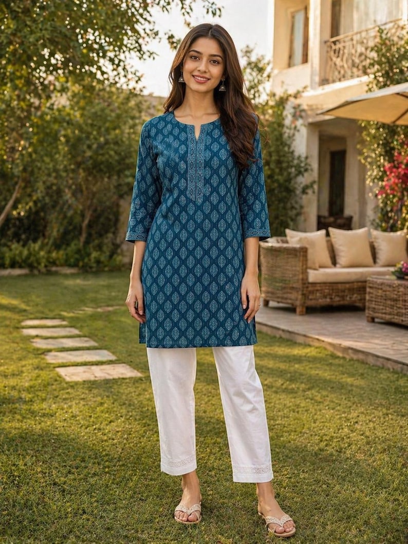 May include: A teal tunic and white pants set. The tunic features a detailed leaf pattern and a split neckline. The three-quarter sleeves and the pants' hem are adorned with a delicate design. The outfit is worn with sandals.