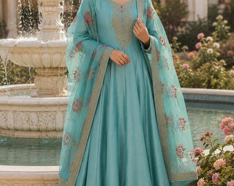 May include: A floor-length teal blue gown featuring a V-neckline with intricate gold embroidery along the bodice and hem. The dress is paired with a matching sheer teal dupatta adorned with delicate floral embroidery and a gold-trimmed border.