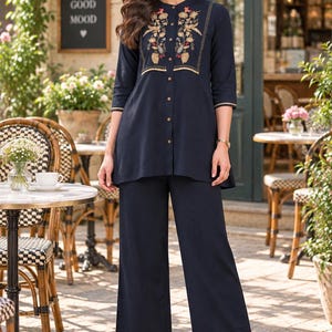 May include: A dark navy blue tunic and wide-leg trousers set. The tunic features a mandarin collar, three-quarter sleeves, a front button placket, and intricate floral embroidery in gold, red, and green tones on the chest with gold trim.