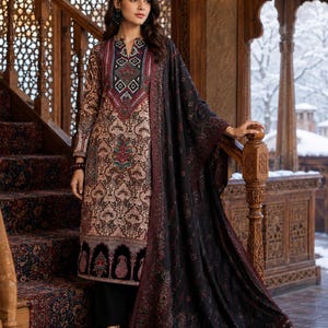 Könnte beinhalten: Ein gemustertes, langärmliges Kleid mit passendem Schal. Das Kleid hat ein detailliertes Design in Braun-, Rot- und Schwarztönen. Der Schal ist über die Schultern drapiert, und das Outfit wird mit einer schwarzen Hose kombiniert. Der Hintergrund ist eine Holztreppe.
