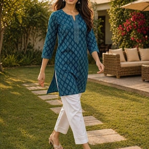 May include: A teal tunic with a leaf pattern and white pants. The tunic has a split neckline and three-quarter sleeves. The white pants are cropped at the ankle. The outfit is worn with sandals.