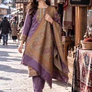Pode incluir: Um conjunto de túnica de manga comprida e calças a condizer em roxo, com um padrão floral decorativo em dourado e azul-petróleo à volta do decote e dos punhos, acompanhado por um grande xaile com franjas e um intrincado padrão paisley.