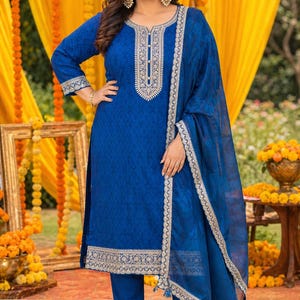 May include: A woman wearing a vibrant blue salwar kameez ensemble. The outfit features intricate embroidery along the neckline, sleeves, and hem. The matching dupatta and pants complete the traditional Indian attire, perfect for festive occasions.
