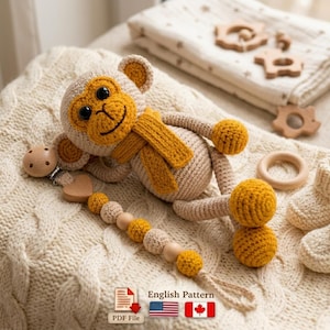 May include: A crocheted monkey toy with a yellow scarf and accents, lying on a cream-colored knitted blanket. A wooden pacifier clip and a beaded chain are attached. The image also includes wooden baby toys and a blanket.