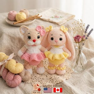 Pode incluir: Duas bonecas de crochê feitas à mão: um gato e um coelho. A boneca de gato usa um vestido rosa e branco com um laço rosa. A boneca de coelho usa um vestido amarelo e branco com um laço amarelo. As bonecas estão em uma toalha de renda.