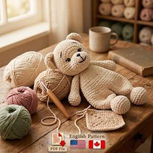 May include: A handmade beige teddy bear lies on a wooden table, surrounded by balls of yarn in cream, pink, and green. A crochet hook and a small crocheted square are also visible. The image includes the text "English Pattern" and a PDF file icon.