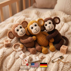 Könnte beinhalten: Drei gehäkelte Affen in Hellbraun, Senfgelb und Dunkelbraun. Jeder Affe hat ein cremefarbenes Gesicht, schwarze Augen und runde Ohren. Enthalten sind zwei Holzklötze mit Herz- und Elefanten-Gravuren, ein Schnullerhalter und eine Sicherheitsnadel.