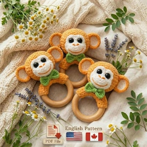 May include: Three handmade crochet monkey baby rattles. Each rattle features an orange monkey face with a white muzzle, black eyes, and a green bow tie. The rattles have wooden rings. The image also includes text that says "English Pattern".