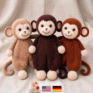 May include: Three crocheted monkey dolls in light tan, dark brown, and medium brown yarn. Each monkey features a cream-colored face, round ears, black plastic eyes, and a stitched smile. A PDF File icon and American and German flag icons are below.