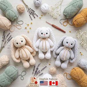 May include: Three handmade crochet bunny toys in cream, white, and gray, each with long ears and a bow. The bunnies are surrounded by yarn in various colors, lavender sprigs, and a crochet hook. The image includes text that says "English Pattern".