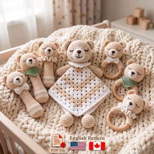 May include: A collection of crocheted bear-themed baby items including a central lovey blanket with a granny square pattern, three rattles with handles, and three teething rings with wooden loops. The items feature beige and white yarn, embroidered closed eyes, and small accessories like bows and green neckerchiefs. A digital icon indicates an English Pattern PDF file.