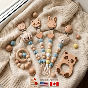 Op de afbeelding: Een verzameling babyaccessoires, waaronder houten fopspeenclips met gehaakte dierenkoppen, een houten bijtring en houten kralen. De clips hebben een kat, beer en konijn ontwerp. De tekst "English Pattern" is ook aanwezig.