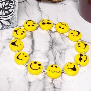May include: A yellow bracelet with silver beads and smiley face charms. Each charm has a different expression.