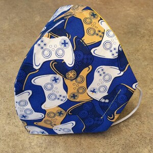 May include: A blue fabric face mask with a white and yellow pattern of video game controllers.