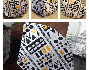 May include: A white face mask with a black and gold geometric pattern. The pattern includes triangles, circles, and squares.
