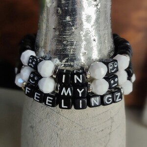 May include: A black and white beaded bracelet with the words "IN MY FEELINGS" spelled out in black beads.