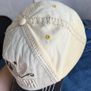 Op de afbeelding: Cr&egrave;mekleurige baseballpet met geborduurde details. Voorzien van een gebogen klep en decoratieve stiksels. De pet heeft een logo met het woord "Dutch" en een ster- en adelaarsontwerp.