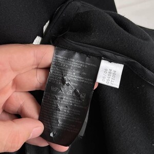 May include: Close-up of a black garment with a tag attached. The tag displays washing instructions and fabric composition, including 65% polyester. The garment's texture is visible, with a focus on the material's weave and construction.