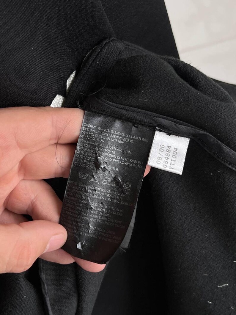 May include: Close-up of a black garment with a tag attached. The tag displays washing instructions and fabric composition, including 65% polyester. The garment's texture is visible, with a focus on the material's weave and construction.