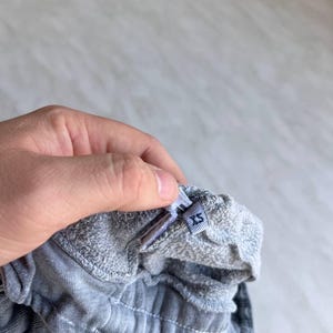 May include: A pair of grey sweatpants featuring an elasticized waistband with visible stitching. A small fabric tag is attached to the interior of the waistband, clearly displaying the size label XS in dark blue text on a light grey background.