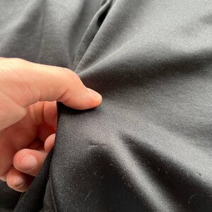 May include: Close-up of black fabric, showing the texture and weave of the material. The fabric is slightly wrinkled, with a few small imperfections visible. The image highlights the details of the textile.