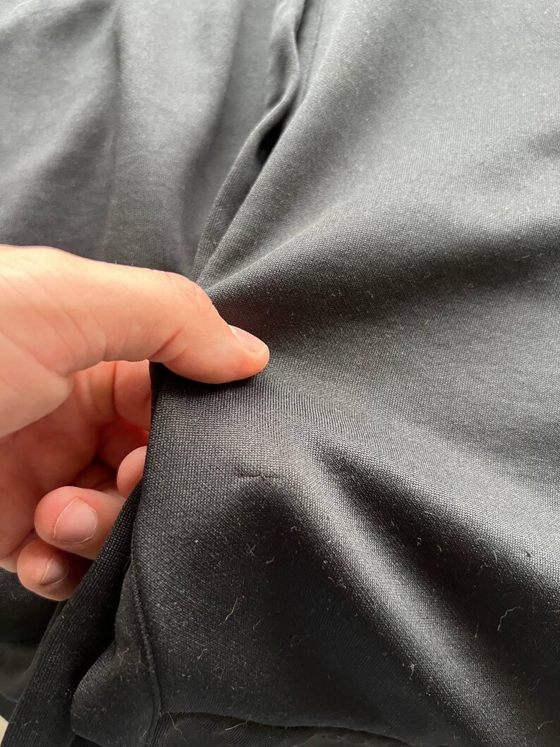 May include: Close-up of black fabric, showing the texture and weave of the material. The fabric is slightly wrinkled, with a few small imperfections visible. The image highlights the details of the textile.