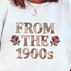Może przedstawiać: Jasnoszara bluza z napisem "FROM THE 1900s" w patchworkowym wzorze. Tekst jest w stylu vintage z kwiatowymi i kratkowanymi wzorami. Czerwone róże znajdują się po obu stronach tekstu.