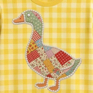 Puede incluir: Camiseta amarilla con estampado de cuadros con un aplique de pato de patchwork. El pato presenta varios patrones de tela, incluyendo fresas y lunares, delineados con perlas de imitación. La camiseta tiene un cuello redondo amarillo.