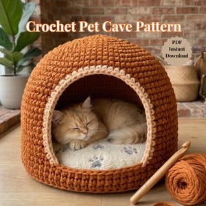May include: A crocheted pet cave in shades of orange and cream, with a sleeping cat inside. The cave has a rounded shape with a contrasting trim around the entrance. The text "Crochet Pet Cave Pattern" is at the top. A crochet hook and yarn are visible.