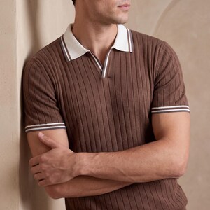 Puede incluir: Polo marr&oacute;n acanalado con cuello y ribete de manga blancos. La camisa tiene cuello en V y mangas cortas. La camisa est&aacute; hecha de un material suave y acanalado.
