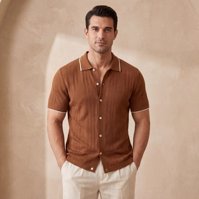 May include: A brown short-sleeve shirt with a textured design and white trim on the collar and sleeves. The shirt is buttoned up and paired with light-colored pants. The overall style is casual and stylish.