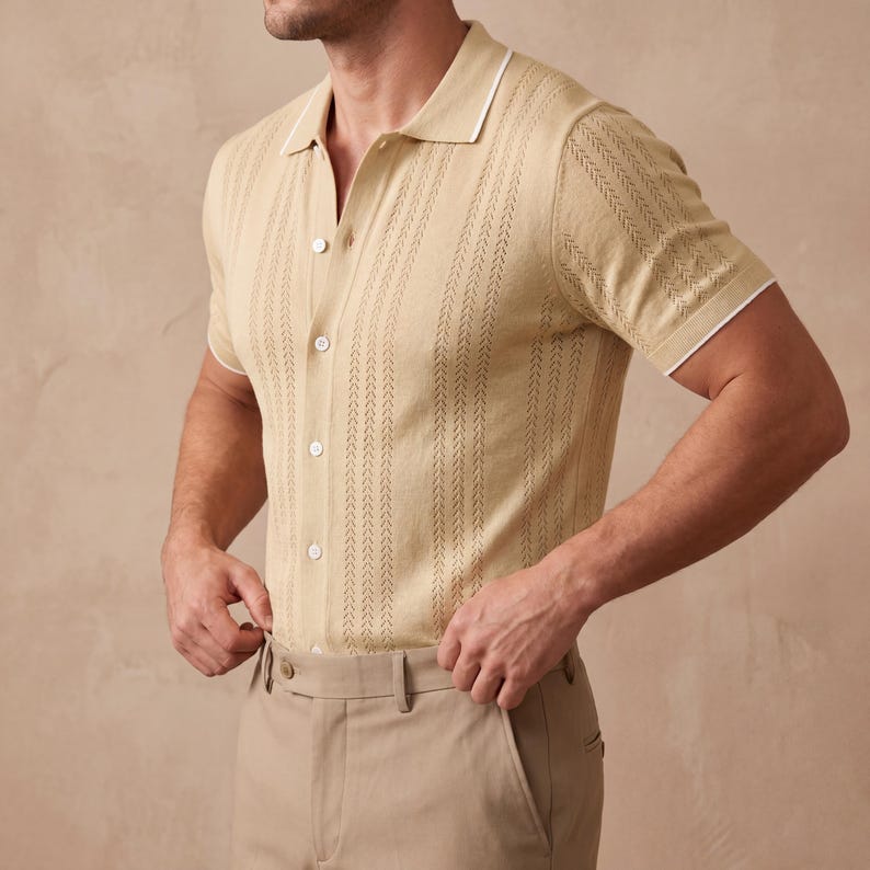 May include: A light tan polo shirt with a textured vertical stripe design. The shirt has a white collar and sleeve trim, and is buttoned up. The model is wearing khaki pants. The shirt is made of a lightweight material.