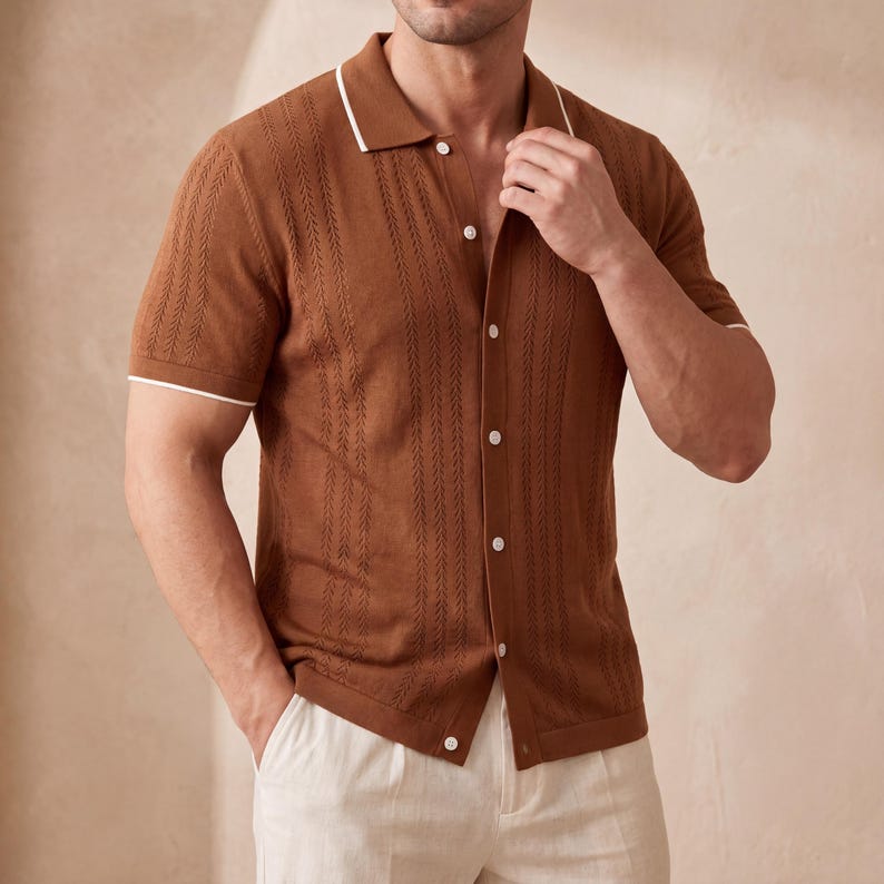 May include: A brown short-sleeved polo shirt with a textured pattern and white trim on the collar and sleeves. The shirt has a button-down front and is paired with light-colored pants. The shirt is made of a knit fabric.