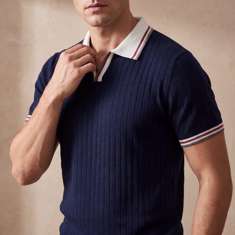 Puede incluir: Polo azul marino acanalado con cuello blanco y ribete rojo y gris. La camisa de manga corta tiene un dise&ntilde;o de rayas verticales texturizadas.