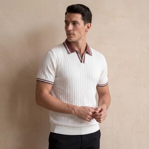 Puede incluir: Polo acanalado color crema con mangas cortas. El cuello y los pu&ntilde;os tienen un ribete burdeos y blanco. La camisa tiene un dise&ntilde;o de cuello en V y se usa con pantalones negros.