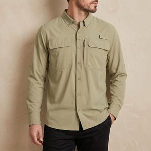 Può includere: Camicia abbottonata a maniche lunghe di colore verde oliva chiaro. La camicia presenta due tasche sul petto, una piccola tasca con cerniera e polsini abbottonati. Il modello indossa pantaloni neri.
